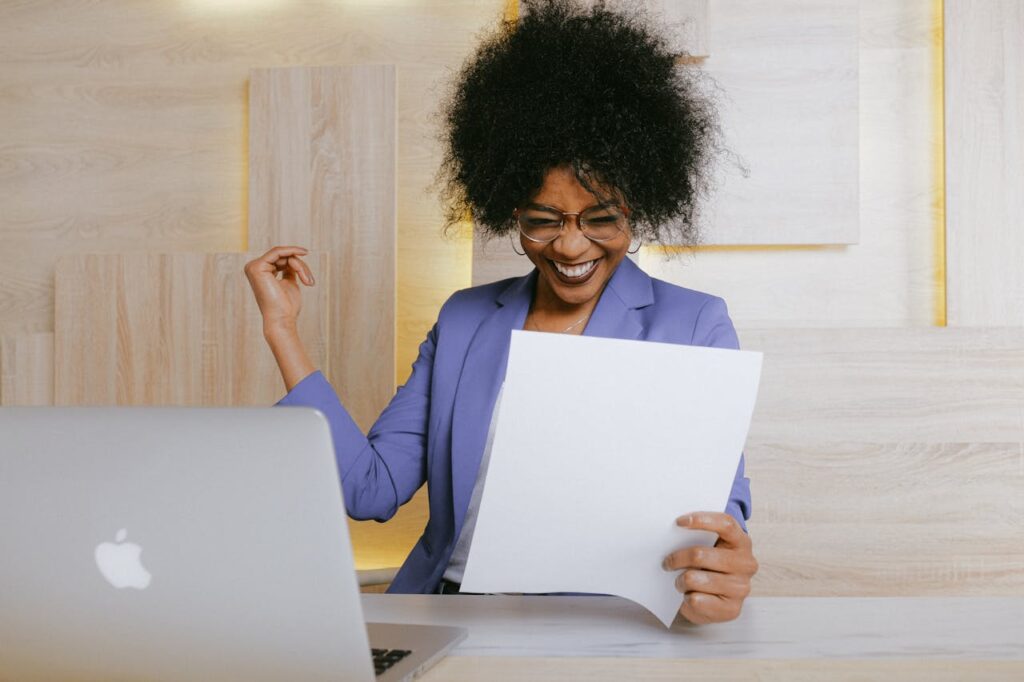 A cheerful woman celebrates her success at work, looking at a document in an office setting.